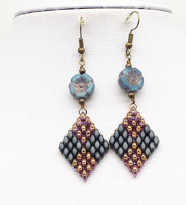 Golden purple and grayish blue diamond shape earrings hanging from a wire wrapped Czech glass blue hibicus bead.